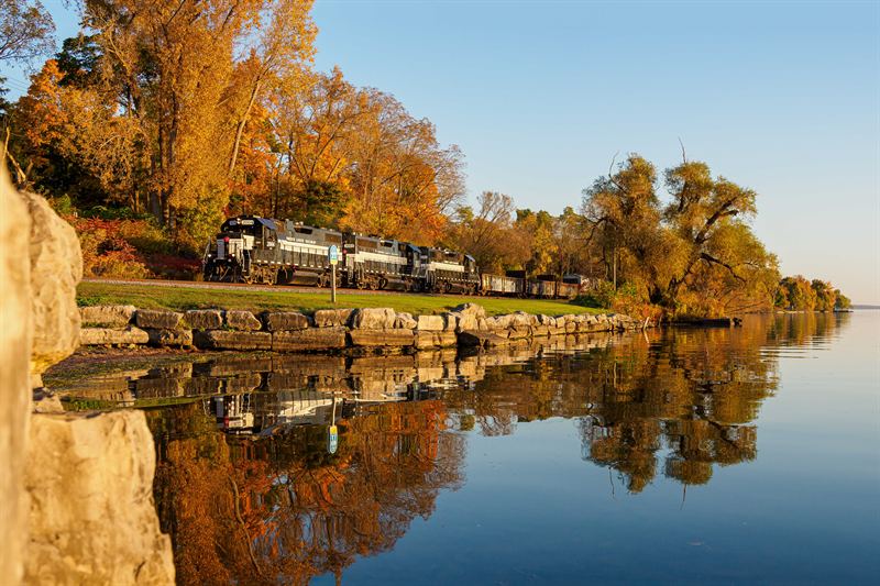 Finger Lakes Railway train along an autumn lakeshore with reflection near Seneca Falls