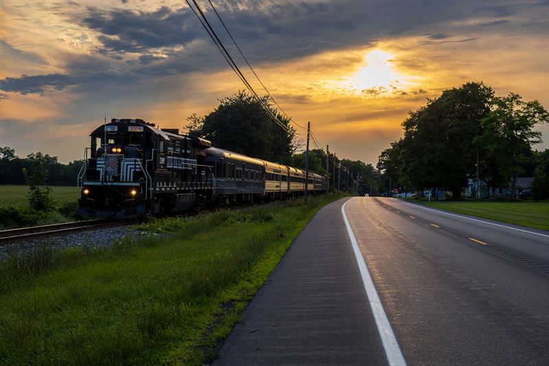 Finger Lakes Railway passenger excursion beside a country road at sunset near Phelps
