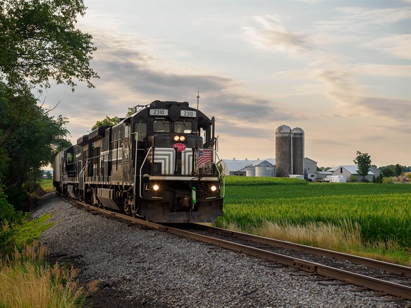 Finger Lakes Railway train passing a farm and silos at dusk near Penn Yan