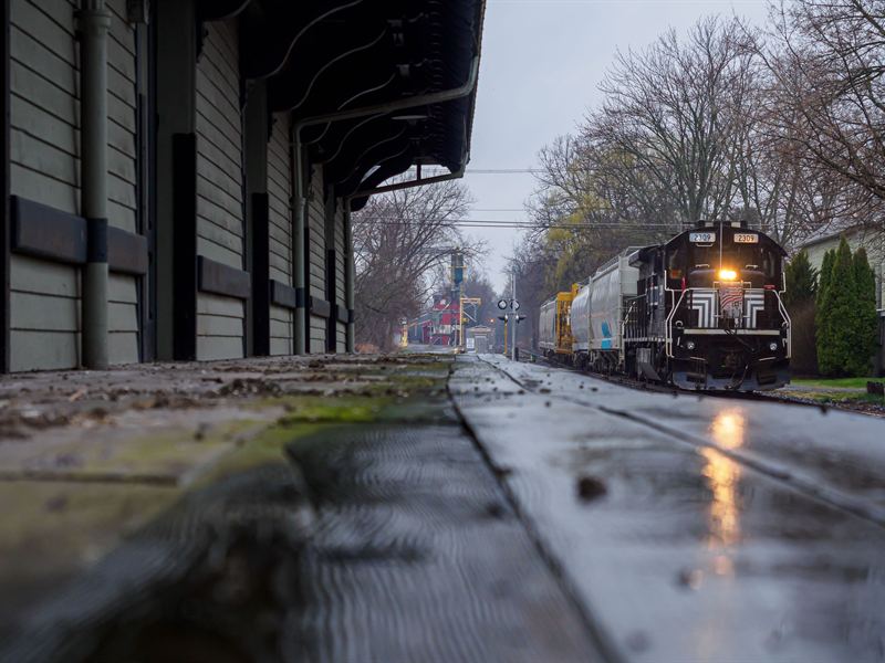 Finger Lakes Railway local passing a rain-soaked depot platform with reflections